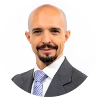 Professional headshot of a bald man with a beard wearing a dark suit and light blue checkered tie